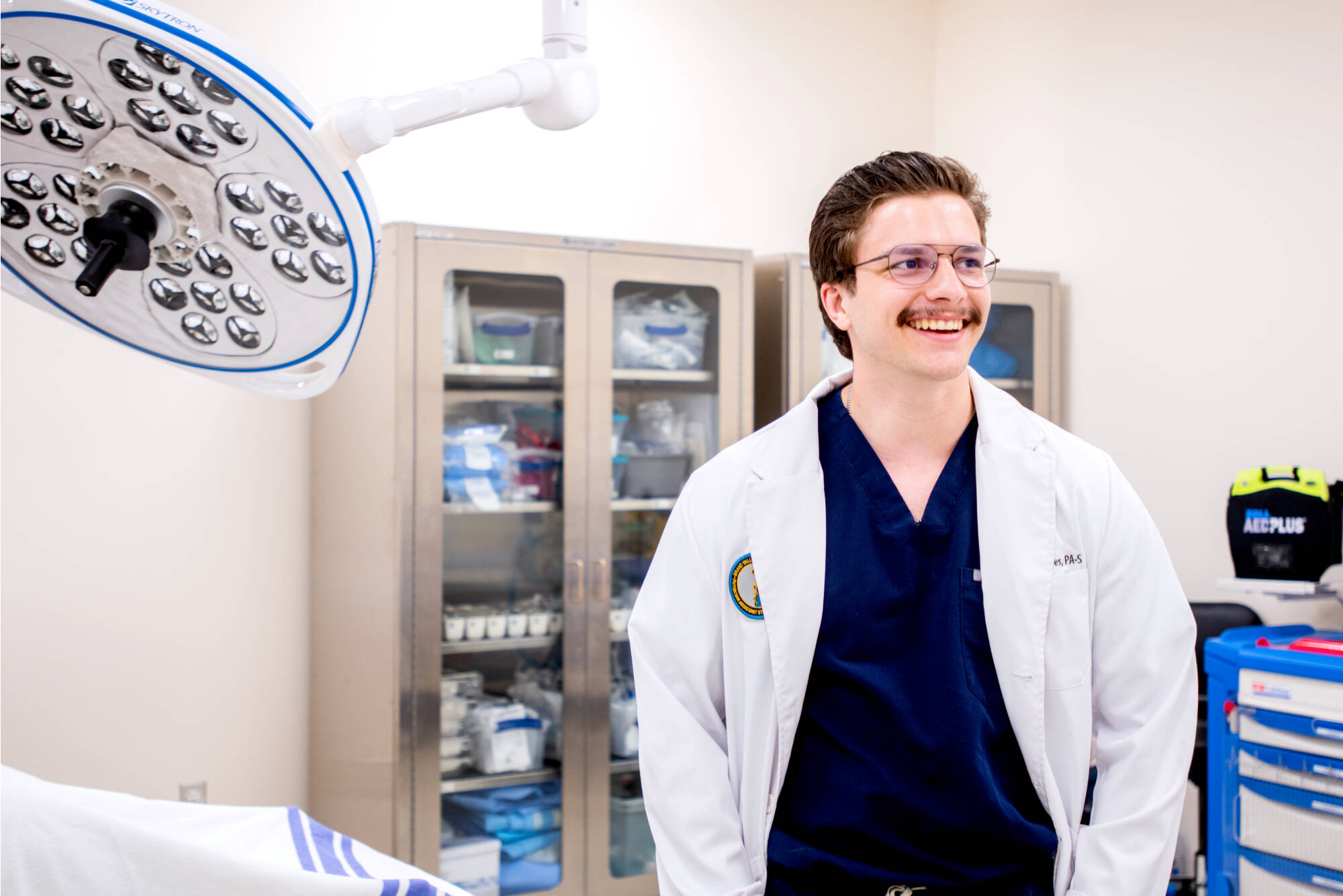 Male student with glasses and a mustache working in an allied health sciences lab.